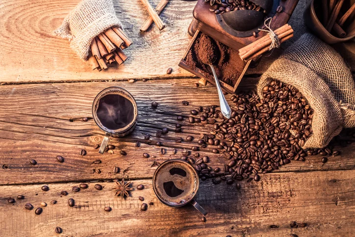 coffee beans in sack scattered over a table next to two cups of coffee.