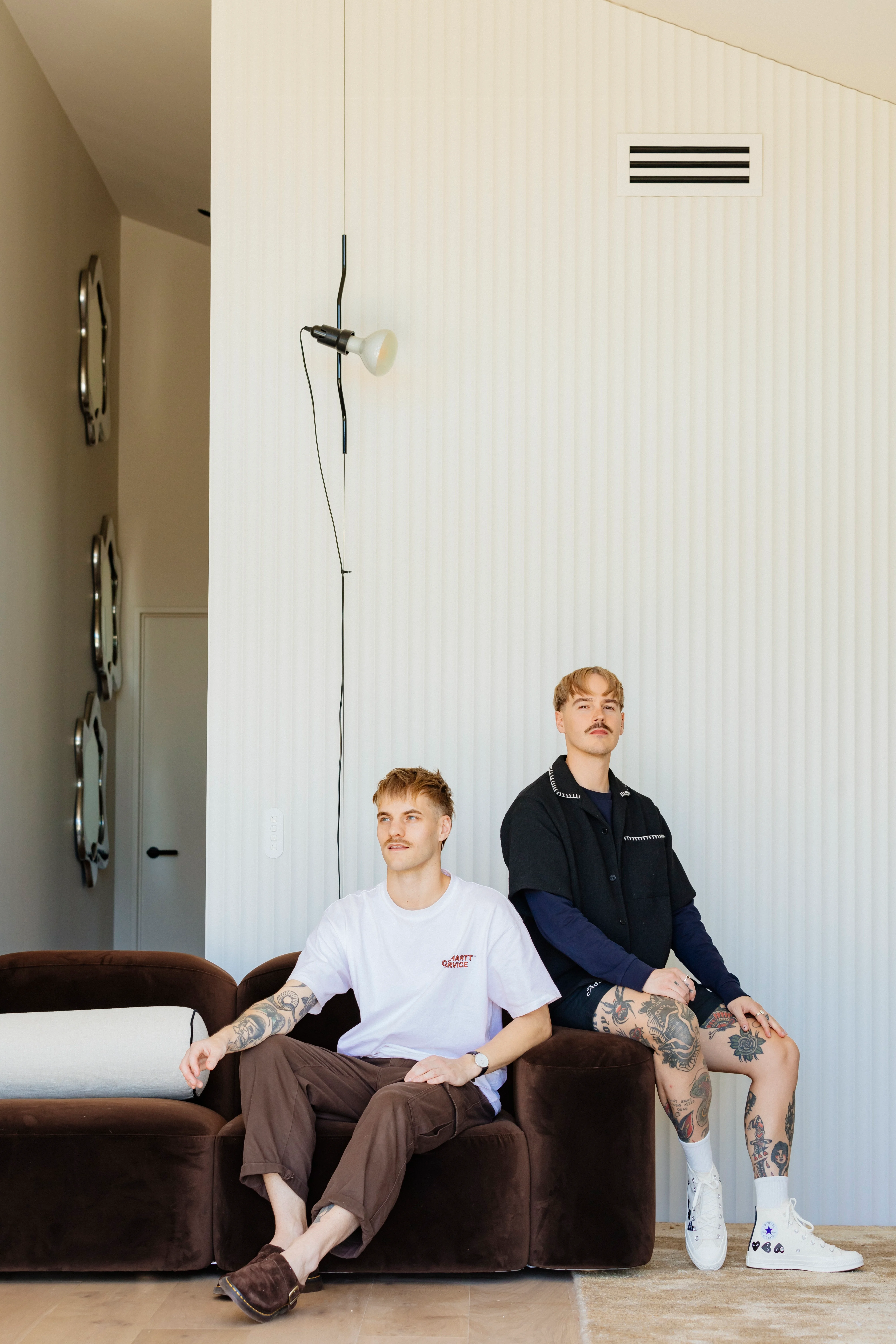 Matt (left) and Dan in their living space, on their Muse sofa by Sarah Ellison, with a trio of Florence mirrors by McMullin & Co and a Parentesi lamp by Flos from ECC suspended beside them