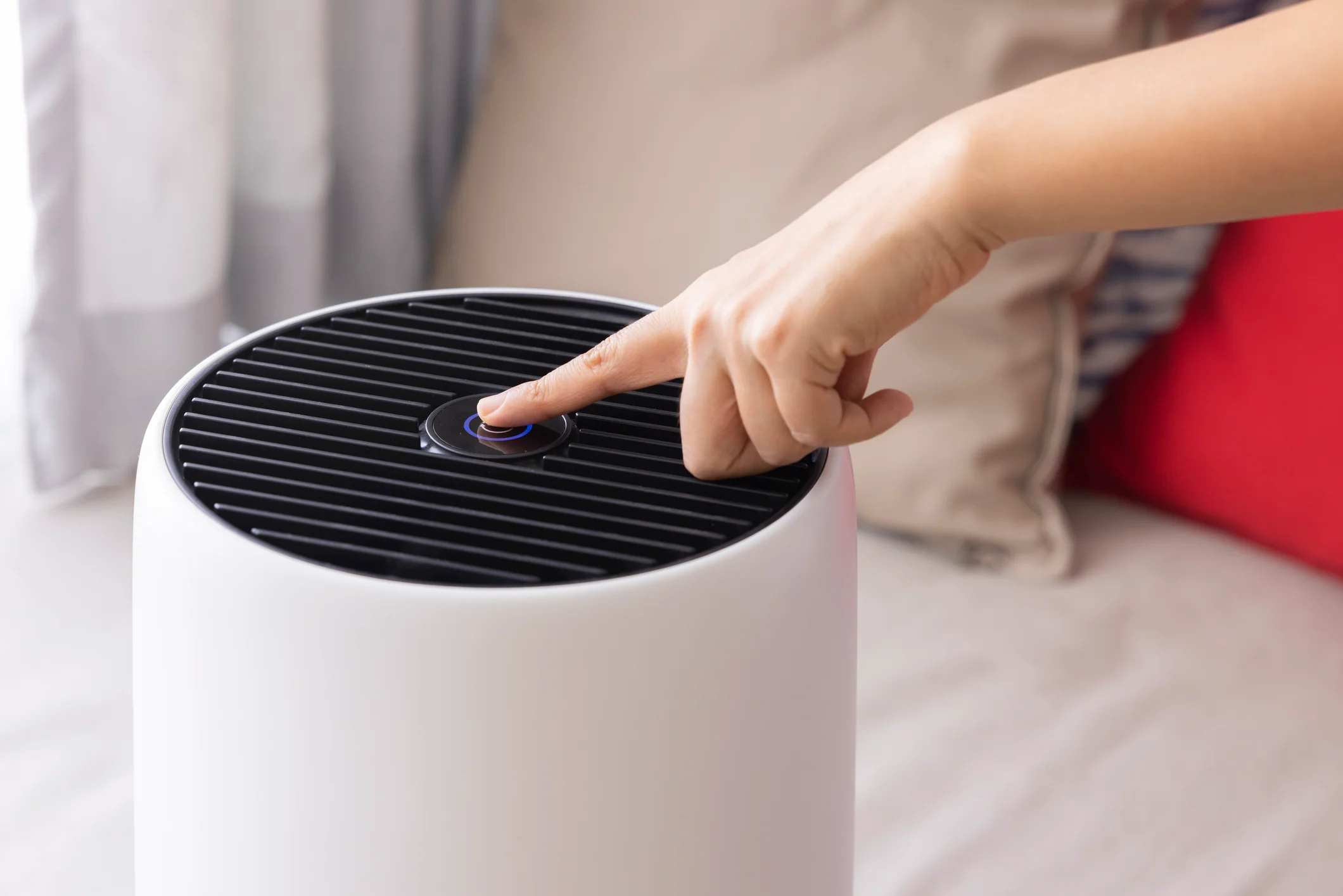 Close up image of a hand pressing a button on a dehumidifier in a bedroom.