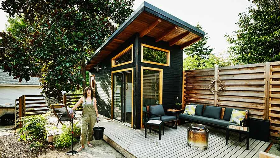 Woman in dungarees standing outside her NZ tiny home.