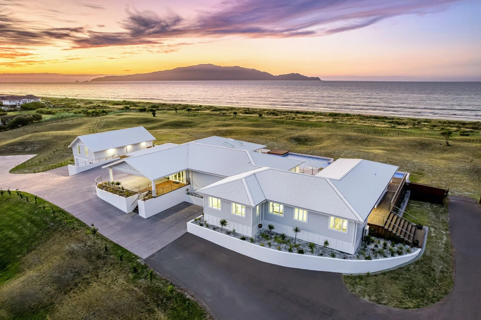 Large modern property sits on the kapiti coast with sunset in the background over the sea.