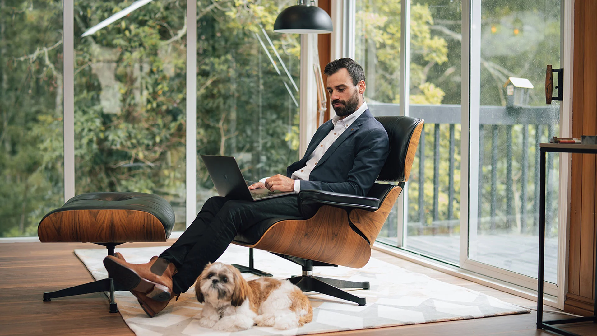 Man sitting in a suit in a chair at home on his laptop reading about saving for a house deposit.