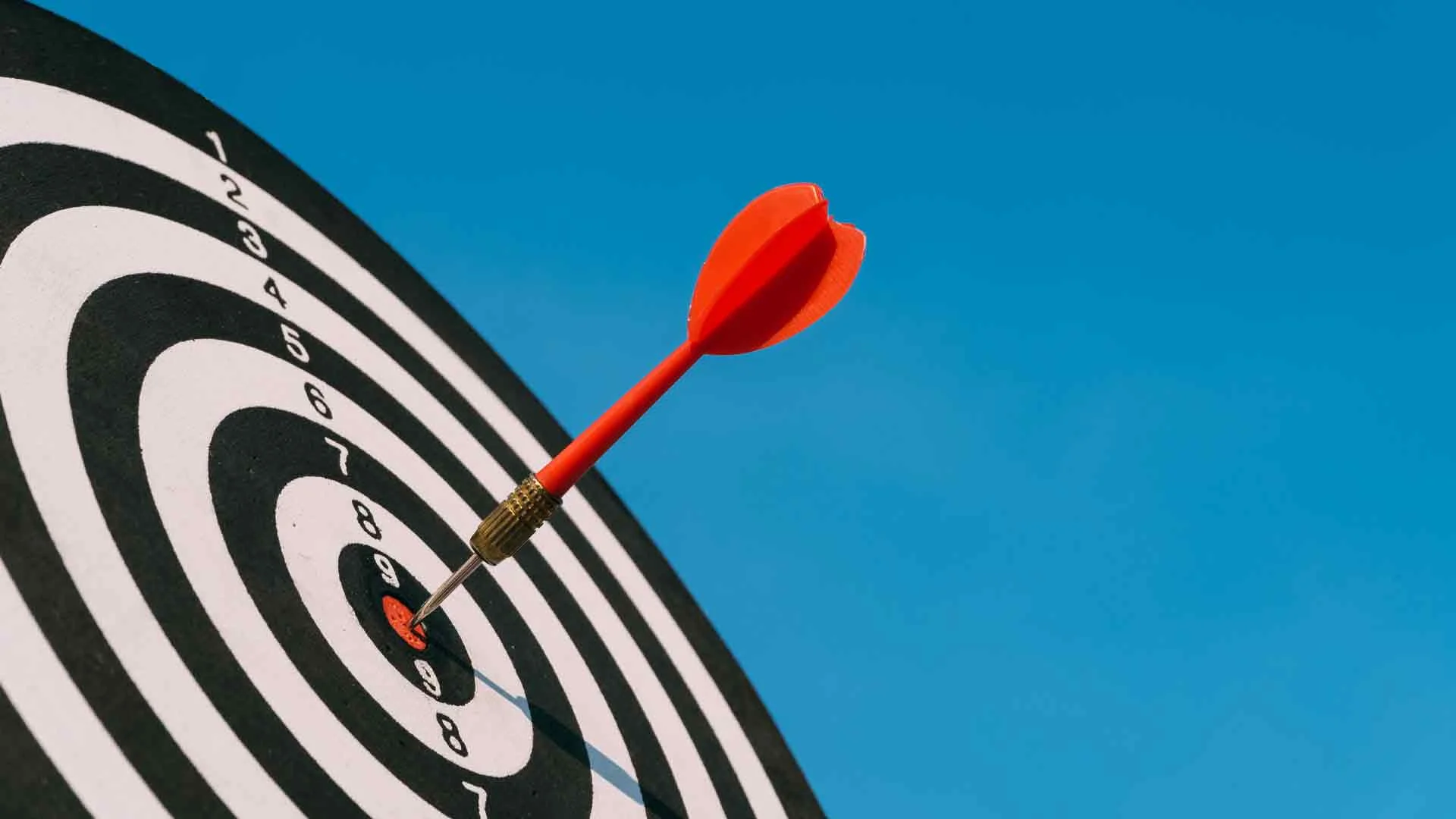Red dart hitting the bull's eye of a dartboard.