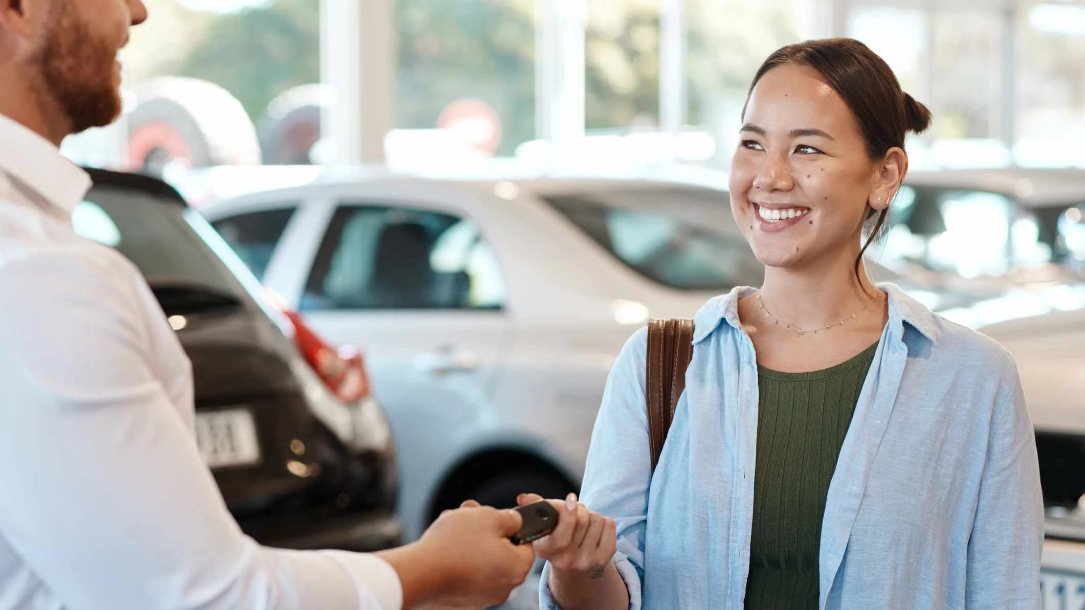 Car salesman handing car key over to female shopper.