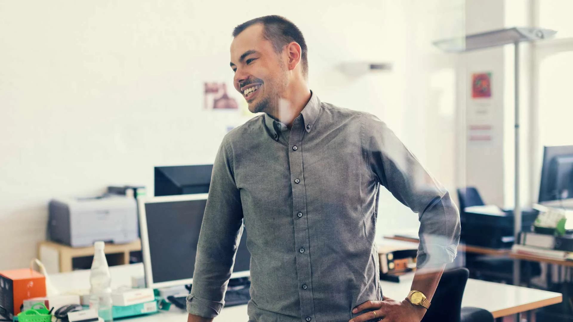 Man standing in a grey shirt in an office.