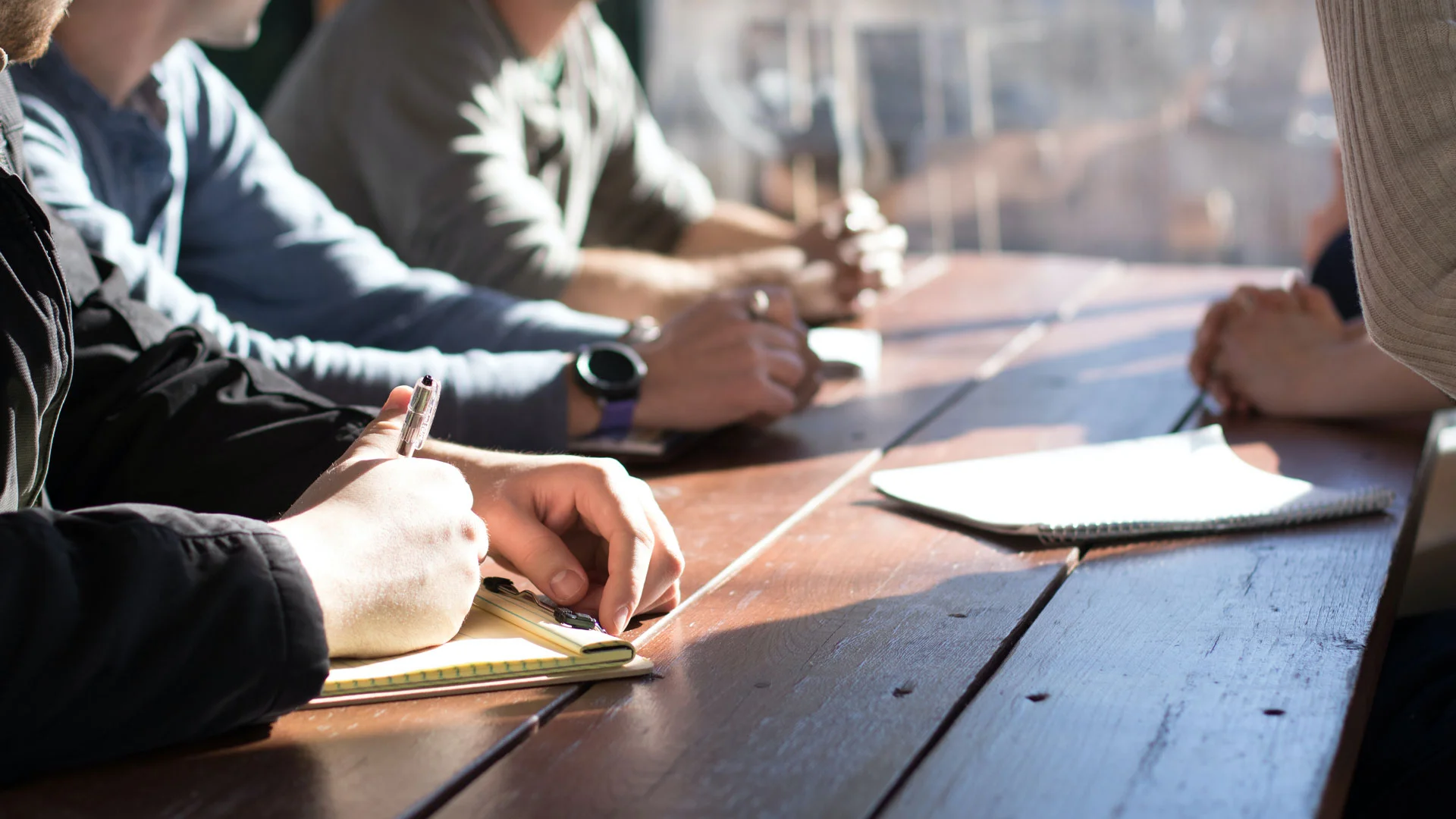 Group of interview candidates sitting at a table with pens and papers taking part in a group interview exercise.