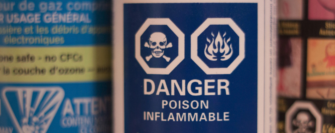 Close up of poisonous hazardous goods label blue back ground with white logos and lettering - features skull and cross bones in a hexagon, beside a flame / flammable logo in a hexagon. Underneath in block letters is written "DANGER", "POISON", "FLAMMABLE"