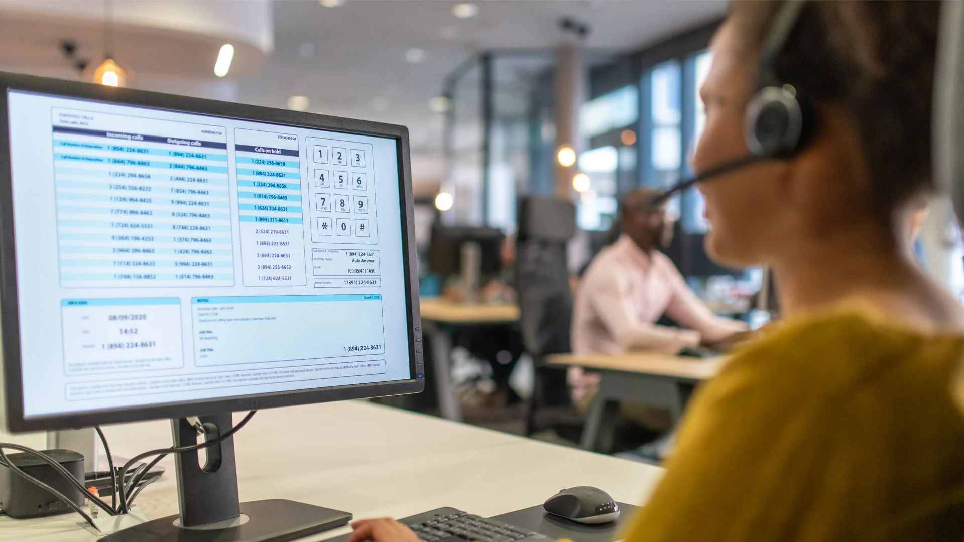 Female customer service representive wearing a headset working on a computer in an office.