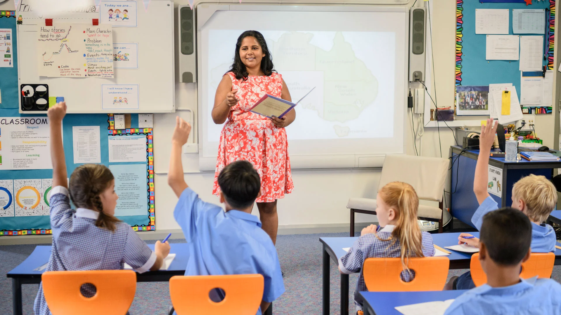 Teacher standing in front of a group of junior school children teaching a lesson.
